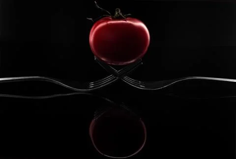 Creative composition of two forks and a red cherry tomato isolated on a black Stock Photos