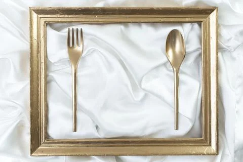 Creative concept of a dinner setting with golden frame, spoon and fork Stock Photos