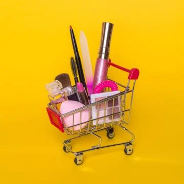 Creative concept with shopping trolley with makeup on a yellow background. Stock Photos