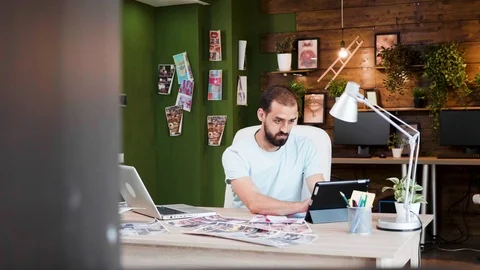 Creative director looking into her tablet and typing on his laptop Stock Footage 113872019
