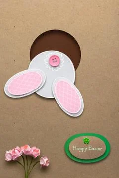 Creative easter concept photo of a rabbit in a hole made of paper on brown backg Stock Photos