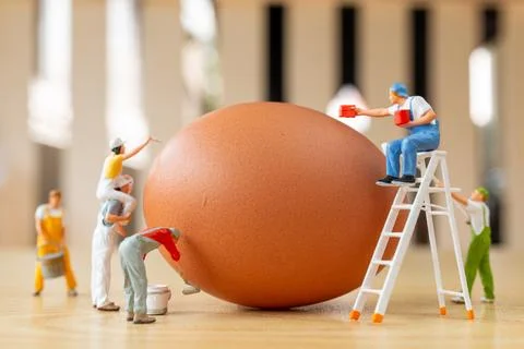 Creative Easter concept with tiny figurines painting a large brown egg Foto stock