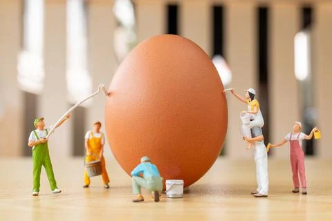 Creative Easter concept with tiny figurines painting a large brown egg Stock-Fotos