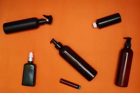 Creative flat lay of dark cosmetic bottles on a bright orange background. Stock Photos