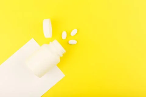 Creative flat lay with opened medication bottle with spilled vitamins on white Stock Photos