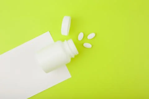 Creative flat lay with opened medication bottle with spilled vitamins on white Stock Photos