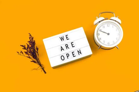 Creative flat lay sign We are open with alarm clock and flowers, top view, bu Stock Photos
