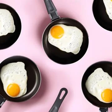 Creative food pattern with fried eggs on pans over pink background. Top view Fotos de archivo