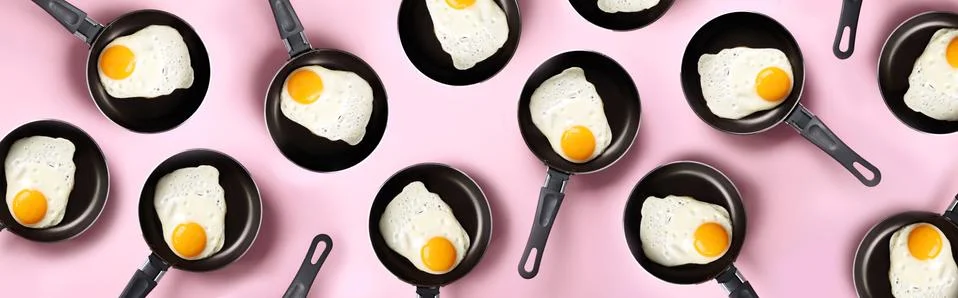 Creative food pattern with fried eggs on pans over pink background. Top view Fotos de archivo