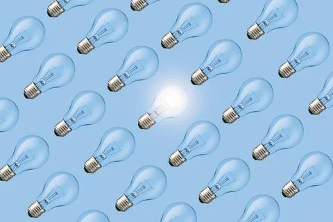 Creative fresh light bulb glowing among many extinguished bulbs on blue bac.. Stock Photos