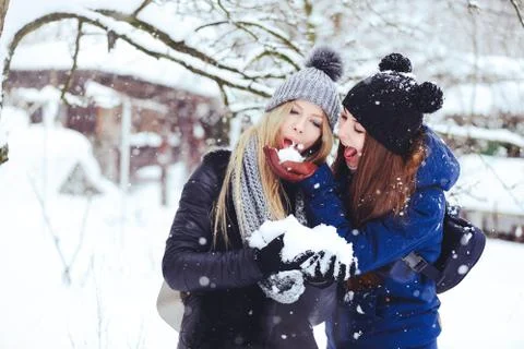Creative funny and happy two beautiful girlfriends play snow in the snow in w Stock Photos