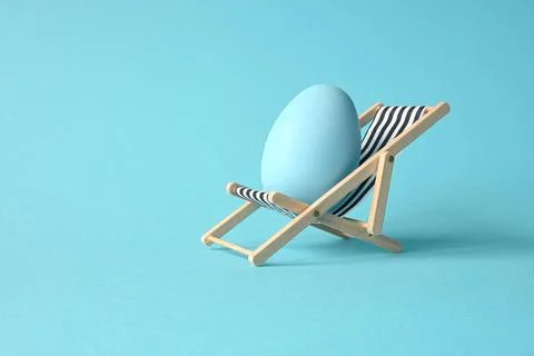 Creative funny composition with Easter egg while sitting on deck chair on pas Stock Photos