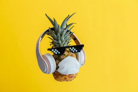 Creative funny pineapple face wearing glasses headphones and protective medical Stock Photos
