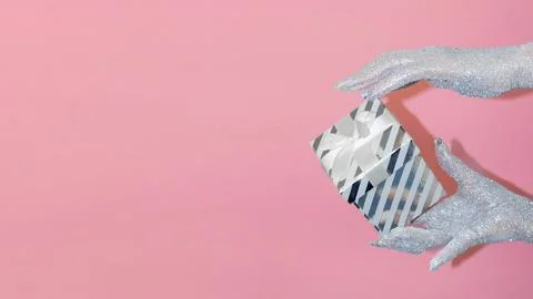 Creative gift wrapping with sparkly hands against a pink background. Stock Photos