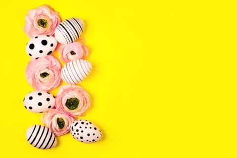 Creative graphic eggs and ranunculus flowers on bright yellow background. Stock Photos