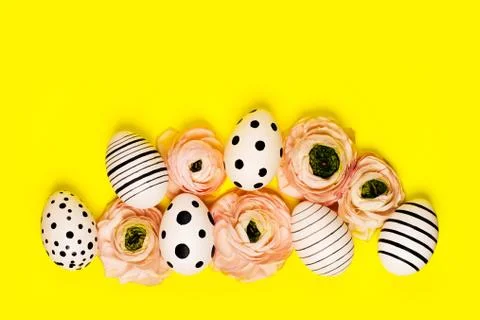 Creative graphic eggs and ranunculus flowers on bright yellow background. Stock Photos