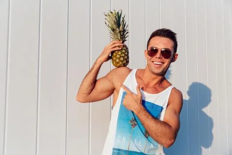 Creative guy holding a pineapple on his shoulder, standing outdoors Stock Photos