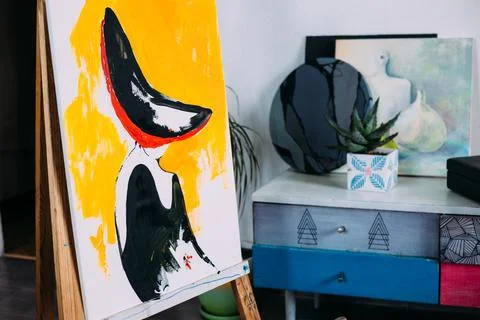 Creative home studio: easel with started painting, paper, painting supplies. Stock Photos