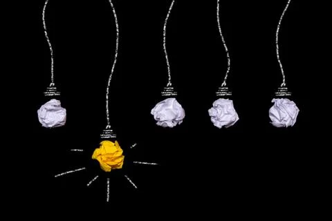 Creative idea of crumpled paper. A burning light bulb on a black background. Stock Photos