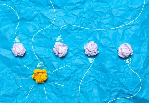 Creative idea of crumpled paper. A burning light bulb on a blue background. Stock Photos