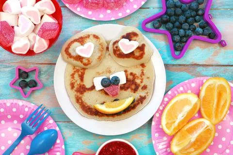 Creative idea for kids breakfast. Bear shaped pancakes on blue wooden table. Stock Photos