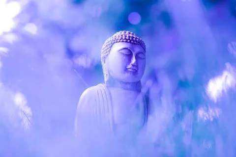 A creative image of a small meditating statue of Buddha on delicate blue-violet Stock Photos