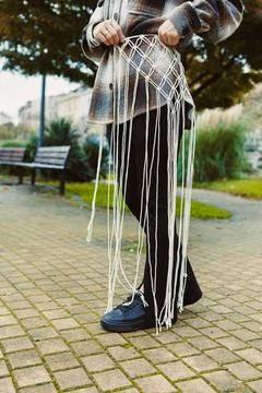 Creative individual displays intricate macrame belt in a park during sunny Stockfoto's