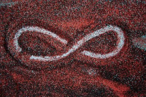 Creative infinity symbol on bright red and black sand background. Stock Photos