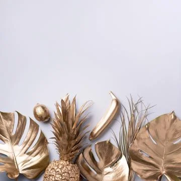 Creative layout. Gold pineapple and golden palm, monstera on grey background Stock Photos