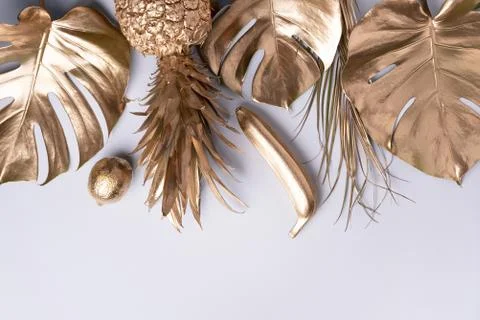 Creative layout. Gold pineapple and golden palm, monstera on grey background Stock Photos