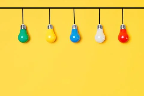 Creative layout with multicolored lightbulbs on yellow background Stock Photos