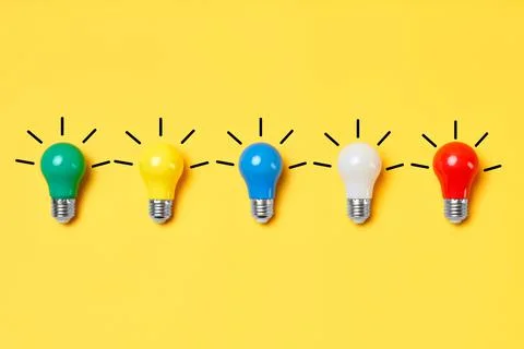 Creative layout with multicolored lightbulbs on yellow background. Stock Photos
