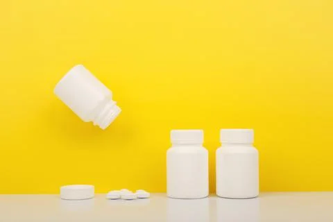 Creative layout with vitamins bottles on white table against yellow background Stock Photos