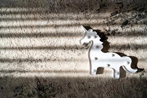 Creative light effect, sunbeam stripes on grey background, white unicorn toy Stock Photos