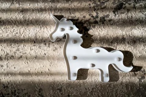 Creative light effect, sunbeam stripes on grey background, white unicorn toy Stock Photos