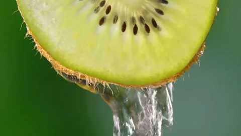 Creative mockup of sliced kiwi slice and water. Splashes on green background. 库存影片 248784013