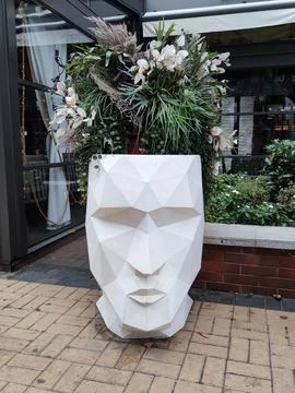 Creative outdoor planter in the shape of a human head with flowers instead of Stock Photos