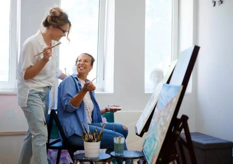 Creative painter and her protege working in a studio Stock Photos