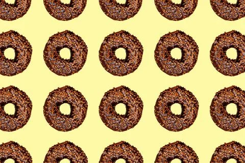 Creative pattern of chocolate donuts with holes on pastel yellow background. Stock Photos