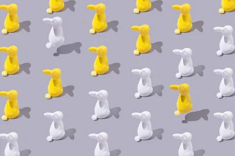 Creative pattern with yellow and white plastic bunny on grey background. Stock Photos