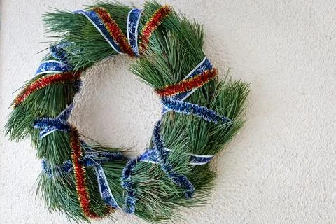 Creative pine wreath adorned with festive ribbons displayed on a white wall.. Foto stock