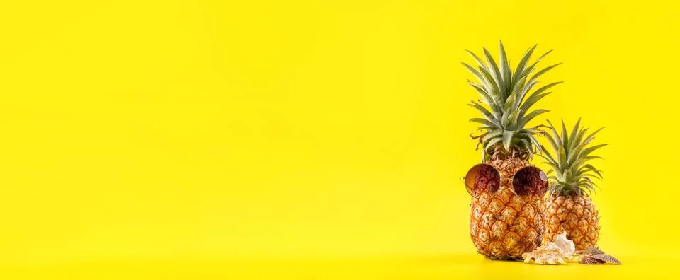 Creative pineapple looking up with sunglasses and shell isolated on yellow ba Stock Photos