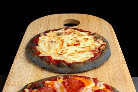 Creative pizza on black dough, two pieces on the board. Фото