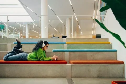 Creative postgraduate student using tablet with headphones in library Foto stock