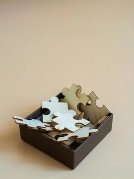 Creative puzzle pieces in brown box on soft beige background for arts and c.. Stock Photos