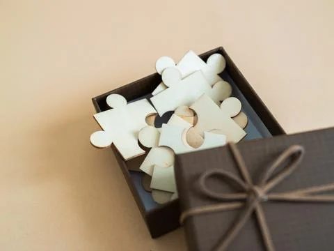 Creative puzzle pieces in a gift box on a soft background for crafting and .. Stock Photos