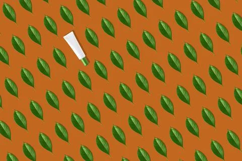 Creative seamless pattern of white cosmetic tube and green leaves on orange Stock Photos