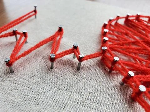 Creative string art project featuring vibrant red yarn and nails on fabric,.. Foto stock
