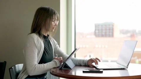 A creative student engages with her tablet while having her laptop ready, in  Stockbeeldmateriaal 275277413