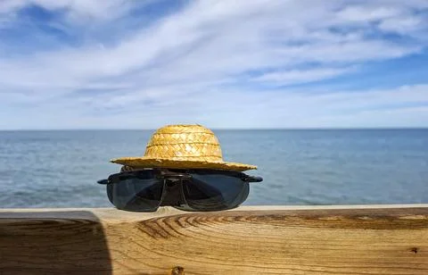 Creative summer scene with straw hat and sunglasses on wooden railing near .. Stock Photos